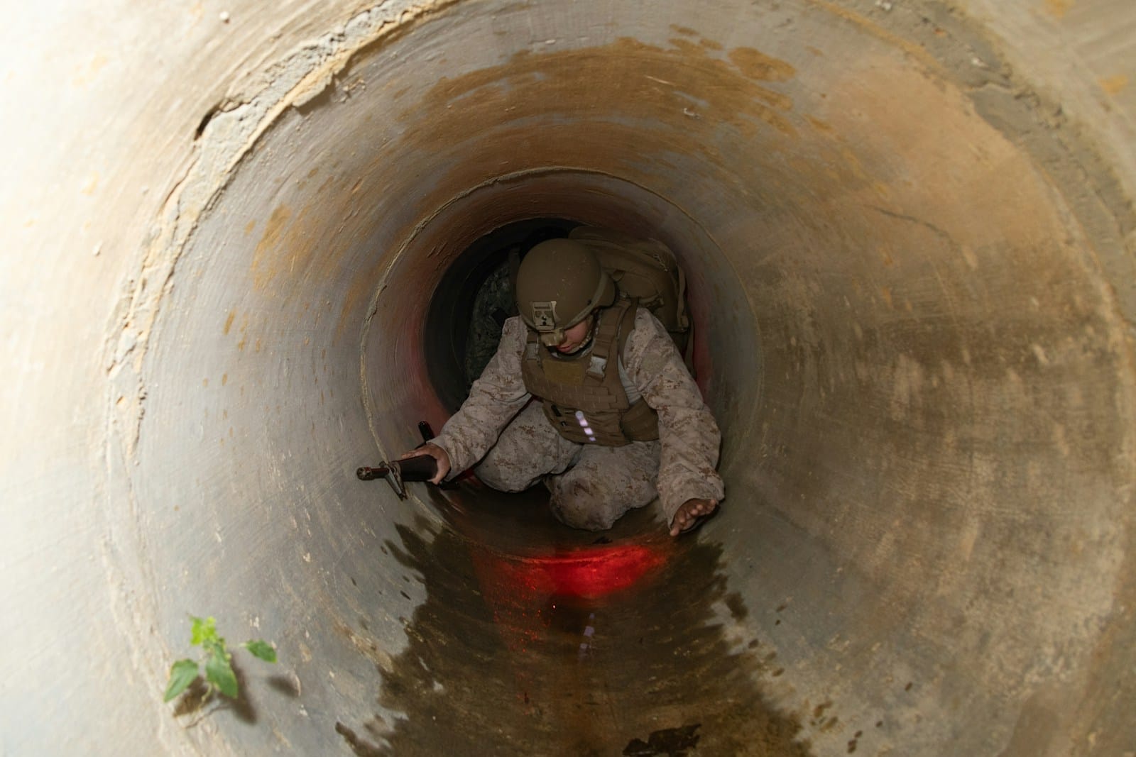 Soldier crawls through a dark, wet tunnel.